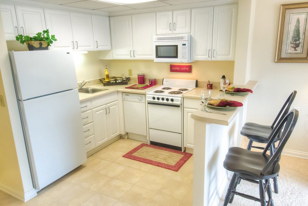 A cozy kitchen with white cabinets, featuring modern appliances and a small breakfast bar.