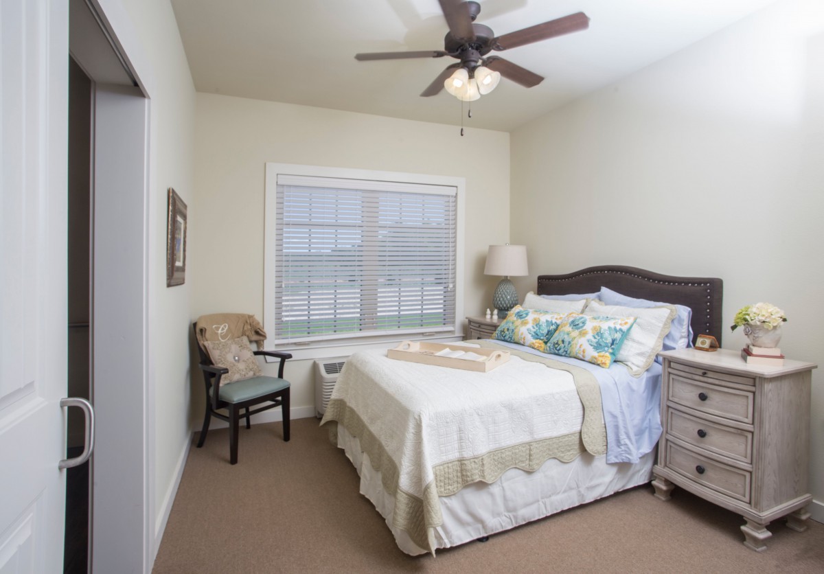 A cozy bedroom with a neatly made bed, ceiling fan, and soft lighting.