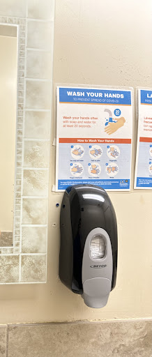 A hand sanitizer dispenser next to a poster displaying proper handwashing techniques.