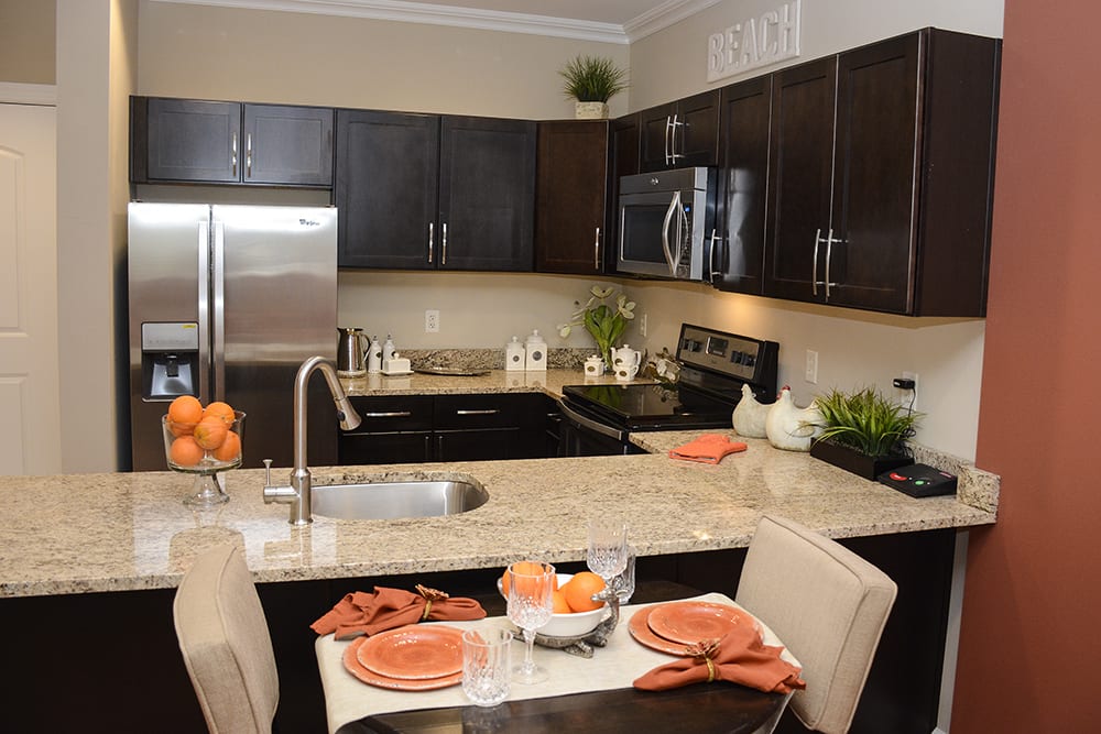 A modern kitchen with stainless steel appliances and a granite countertop, featuring a small dining area with orange-themed decor.