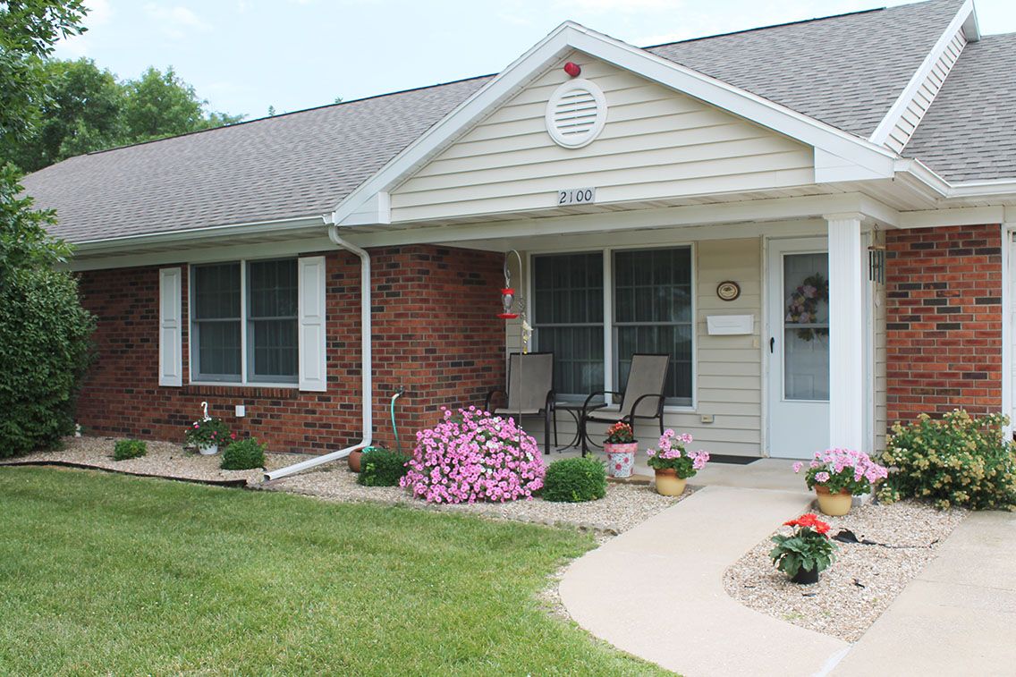 A charming house with a well-maintained front yard and garden, featuring flower pots and patio chairs on the porch.