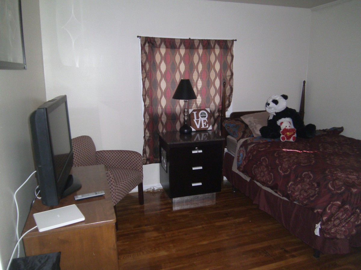 A cozy bedroom with a bed, nightstand, TV, and a panda plush toy sitting on the bed.