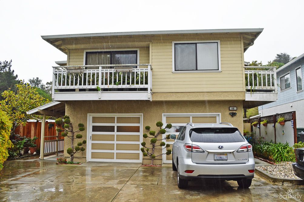 A two-story residential house with a garage and car parked in the driveway on an overcast day.
