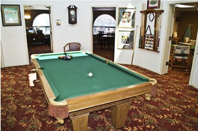 A cozy game room featuring a pool table with a green felt surface and ornate carpeting.