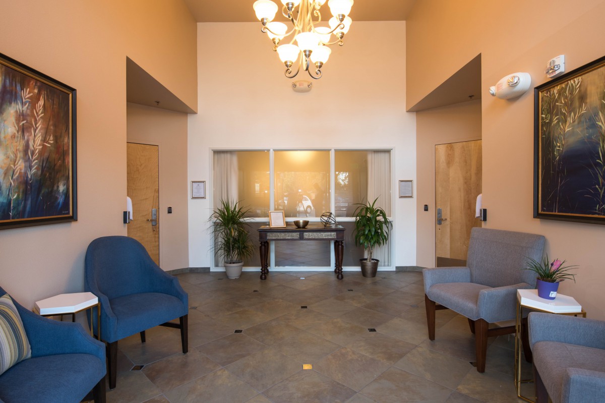 A well-lit lobby with blue chairs, plants, and a chandelier.