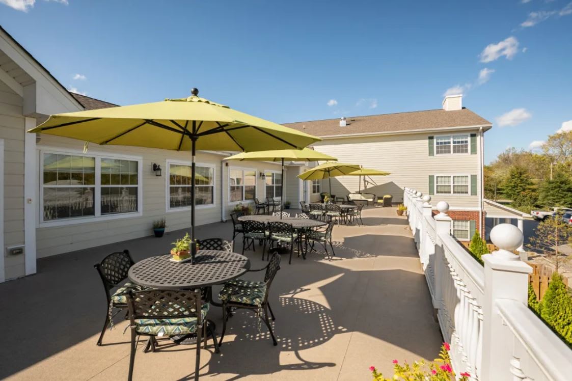 A sunny outdoor patio area with tables, chairs, and umbrellas beside a building.