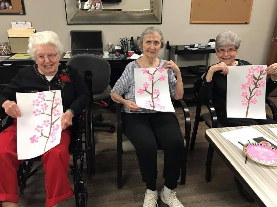 A group of elderly individuals proudly display their artwork during a painting activity.
