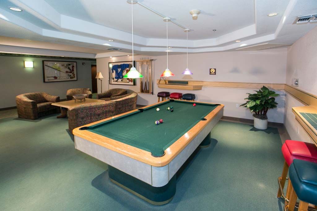 A well-lit game room featuring a billiards table and comfortable seating.