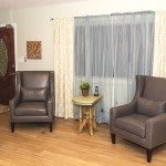 A cozy living room with two leather armchairs, a small table, and light curtains.