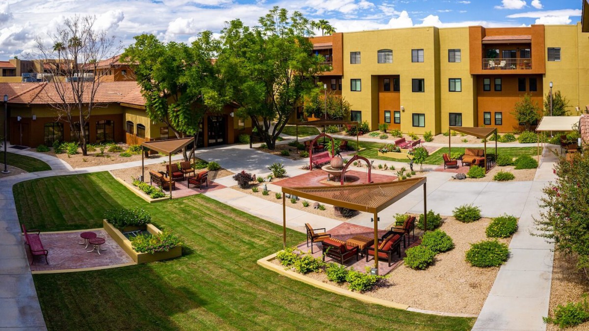 A beautifully landscaped courtyard with seating areas and lush greenery in front of a multi-story building.
