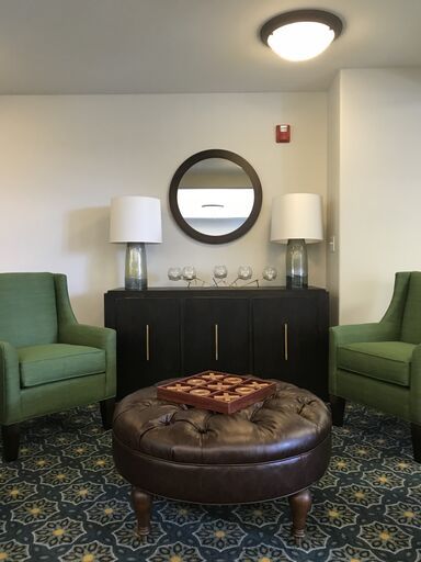 A cozy living room setup with green chairs, a round coffee table, and a mirror above a sideboard flanked by lamps.