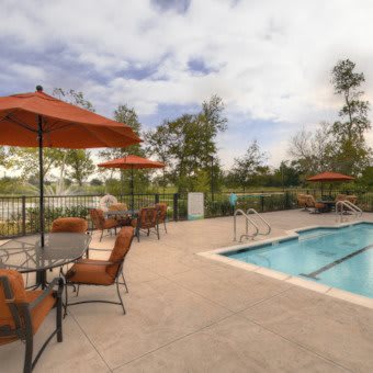 An outdoor swimming pool area with patio furniture and umbrellas, surrounded by trees under a cloudy sky.
