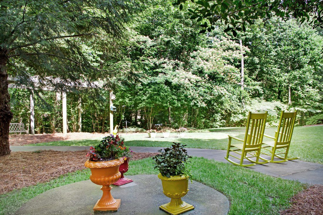 A tranquil outdoor patio with colorful potted plants and a yellow rocking chair overlooking lush greenery.