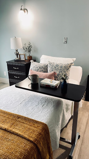 A cozy bedroom setup featuring a neatly made bed, decorative pillows, a bedside table with a lamp and books, creating a tranquil atmosphere.