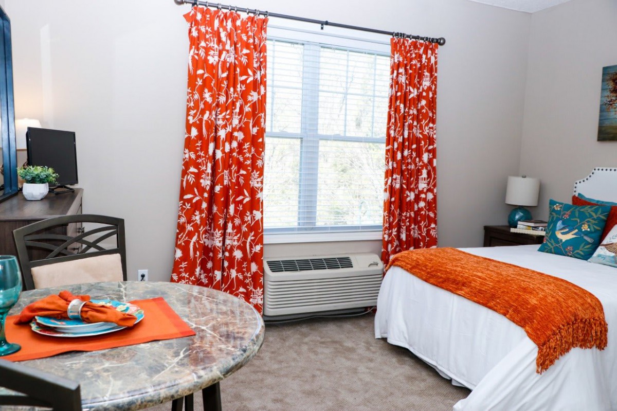 A cozy bedroom featuring vibrant orange curtains and a neatly made bed.