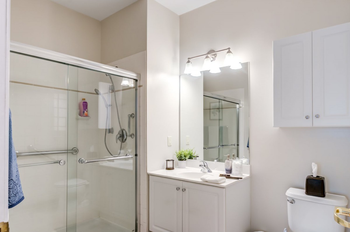 A modern and clean bathroom with a glass shower, large mirror, and neatly organized sink.