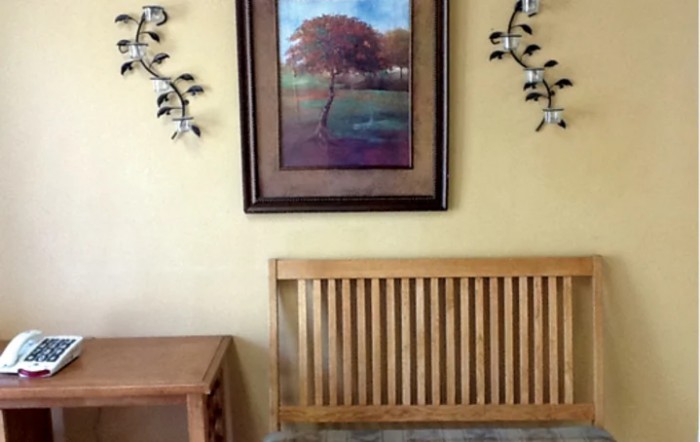 A cozy interior with a framed landscape painting, decorative wall accents, a wooden bench, and a side table.