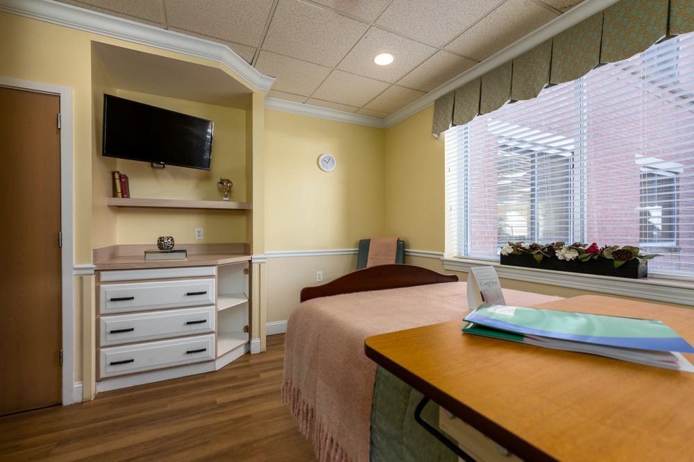 A cozy bedroom with a single bed, a wall-mounted television, and a window providing natural light.