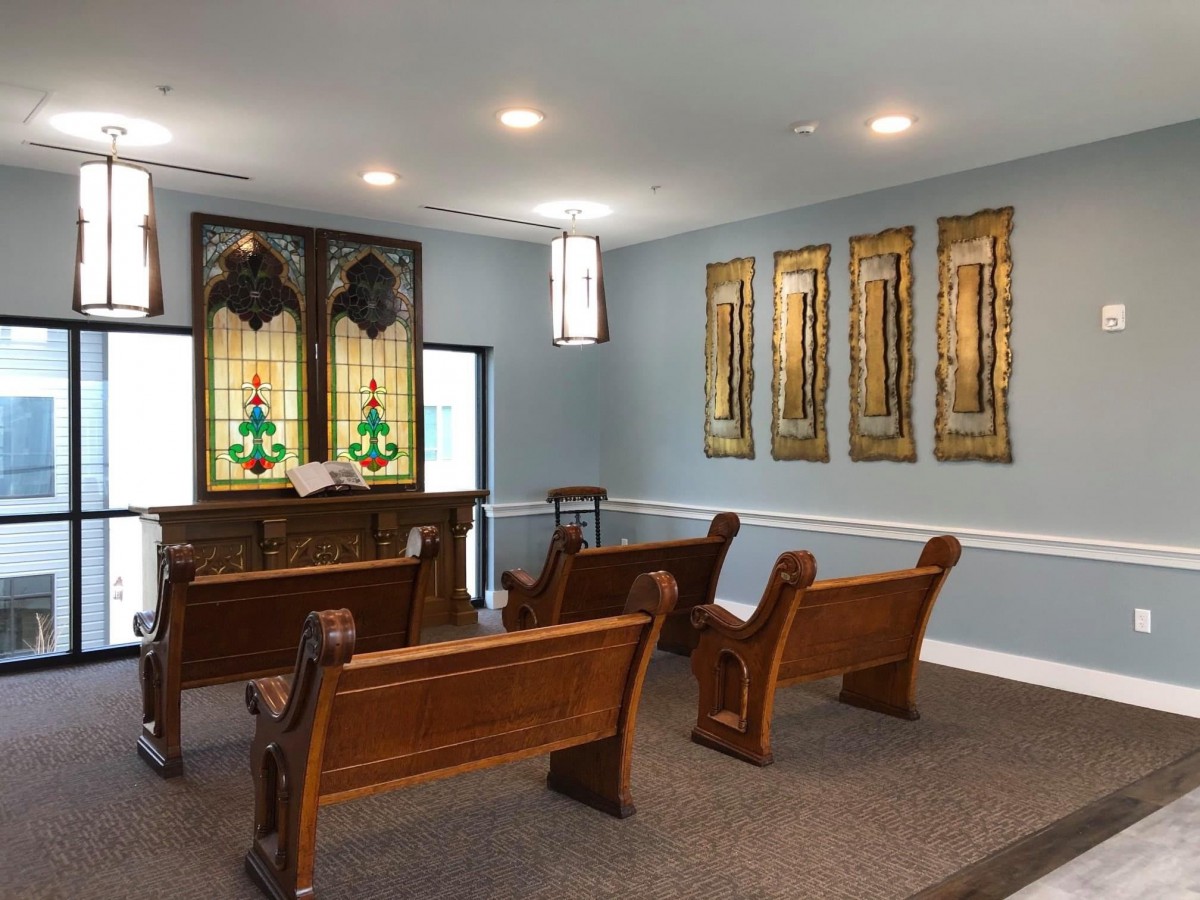 An interior view of a small chapel with wooden pews and stained glass windows.