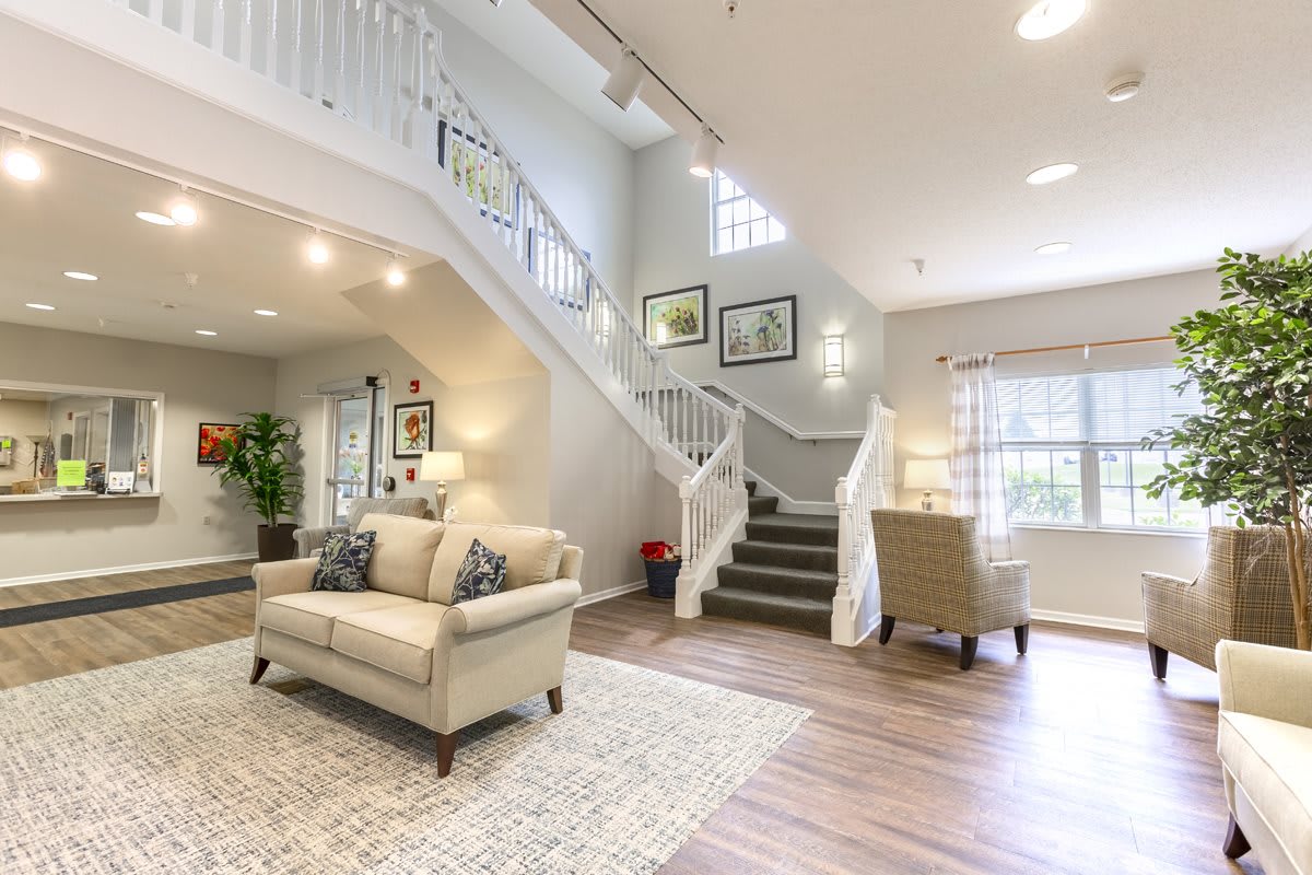 A spacious and well-lit living room featuring a modern design with a cozy sofa, elegant staircase, and large windows.