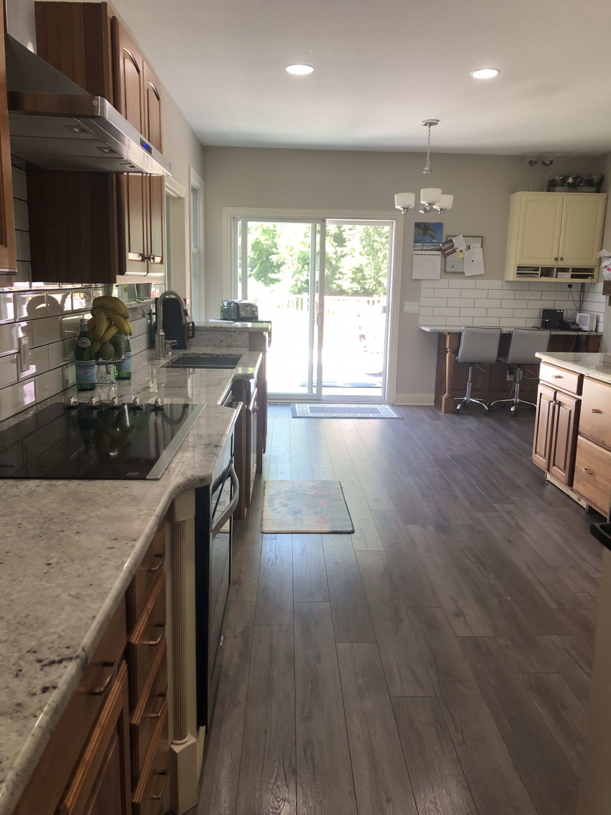 A modern kitchen with wooden cabinets, a sleek countertop, and hardwood floors leading to a dining area with natural light through sliding doors.