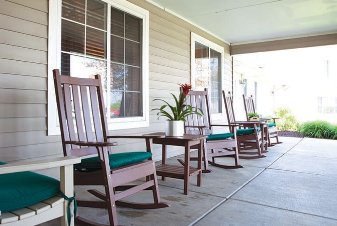 A serene porch featuring wooden rocking chairs and a small table with a potted plant, perfect for relaxation.