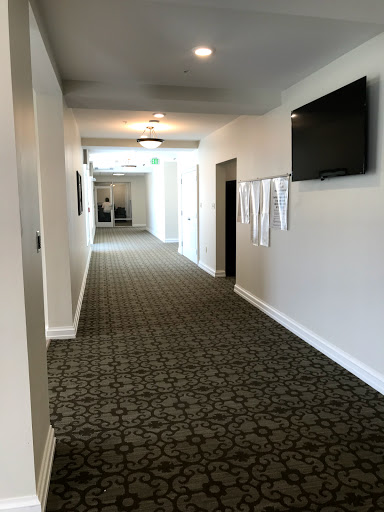 A well-lit hallway with patterned carpet and a wall-mounted television.