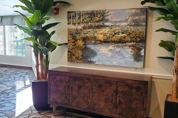 A cozy interior space featuring a large landscape painting above a wooden cabinet, with a potted plant nearby.