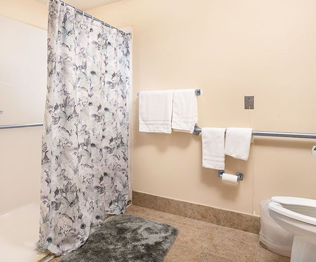 A clean and organized bathroom with a floral shower curtain, neatly arranged towels, and a gray bath mat.