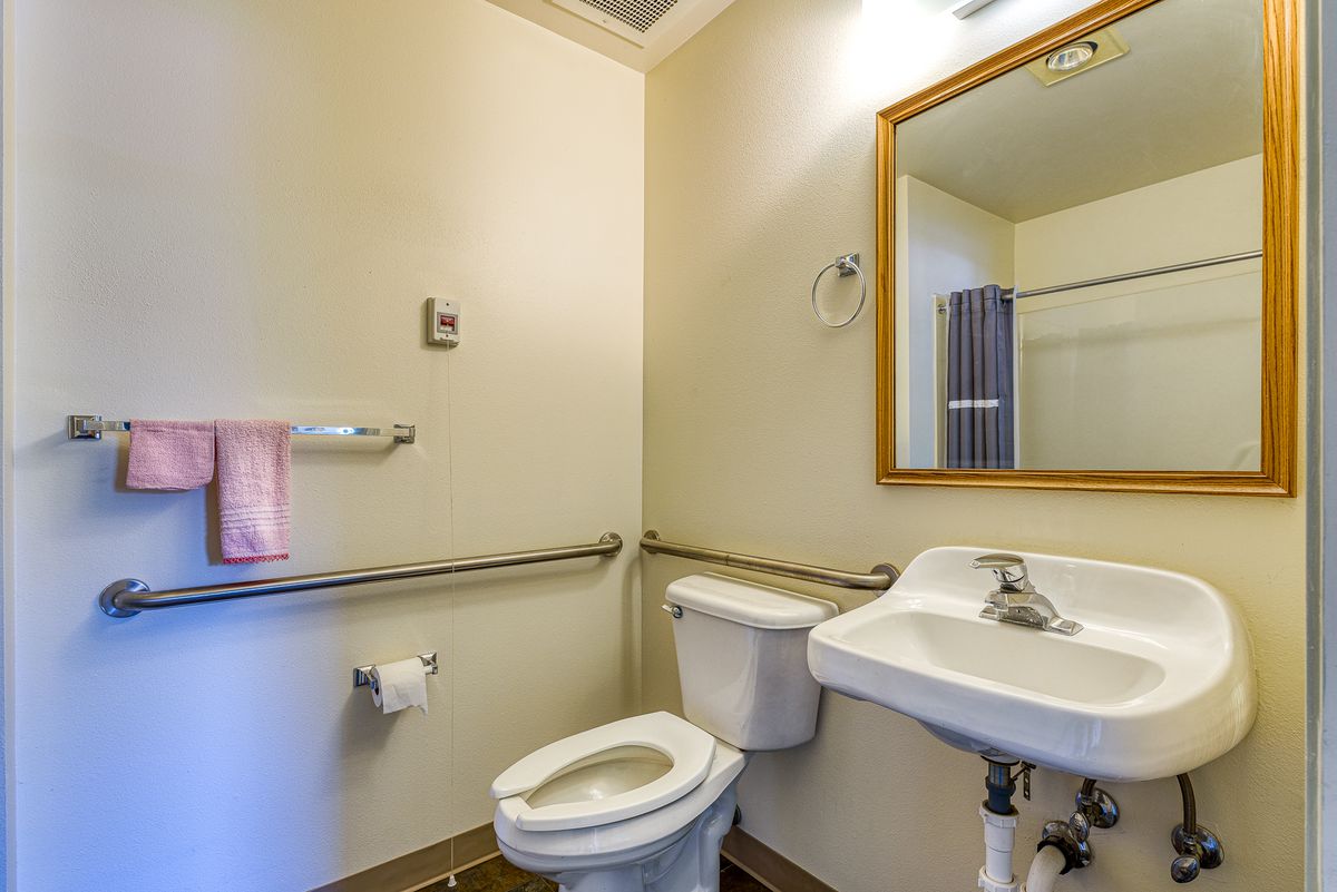 A small bathroom featuring a toilet, sink, and mirror with accessibility handrails.