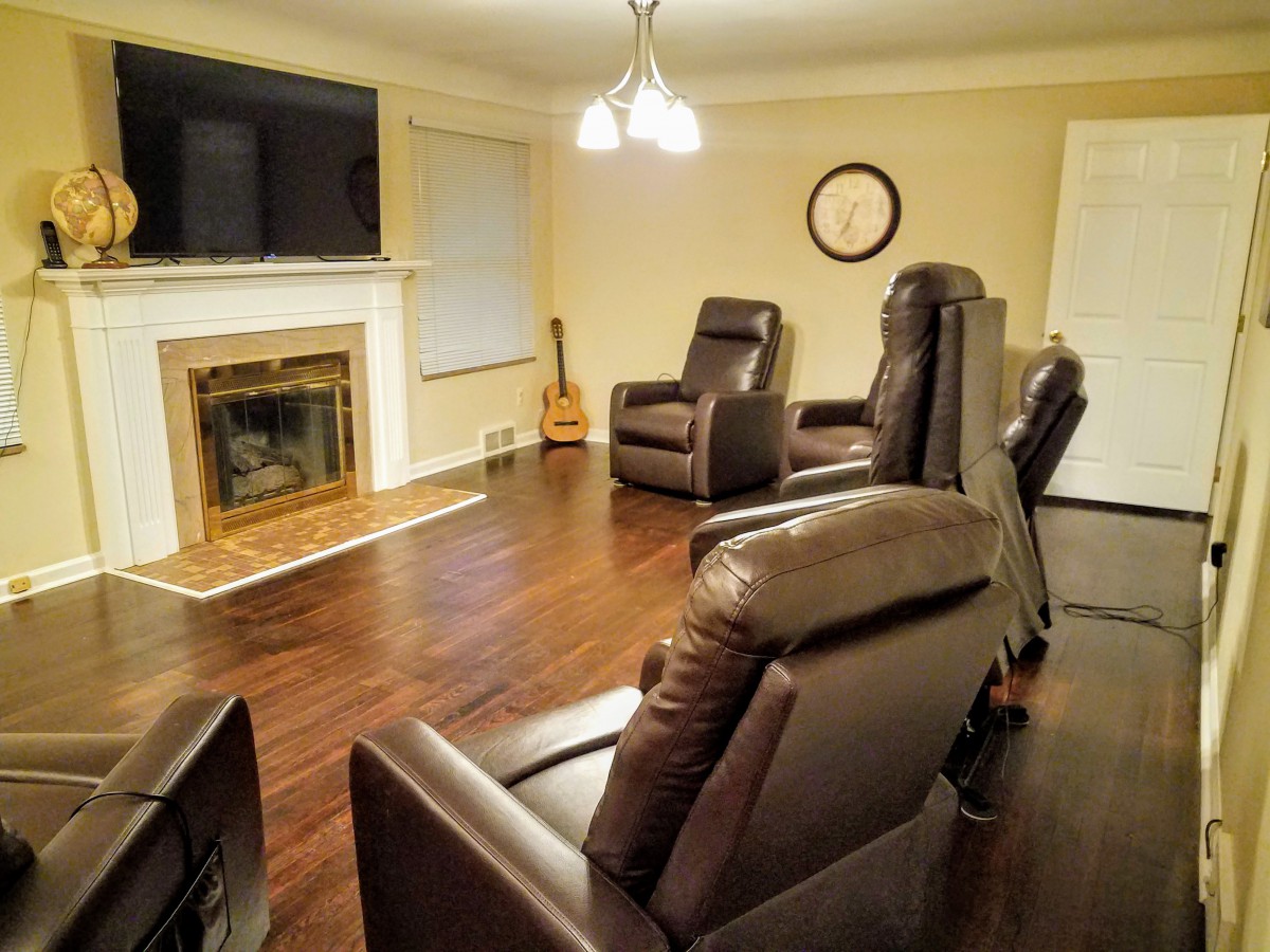 A cozy living room with leather recliners arranged around a fireplace and television, featuring warm wood flooring and a guitar in the corner.