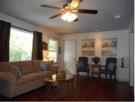 A cozy living room with a sofa, chairs, and a ceiling fan.