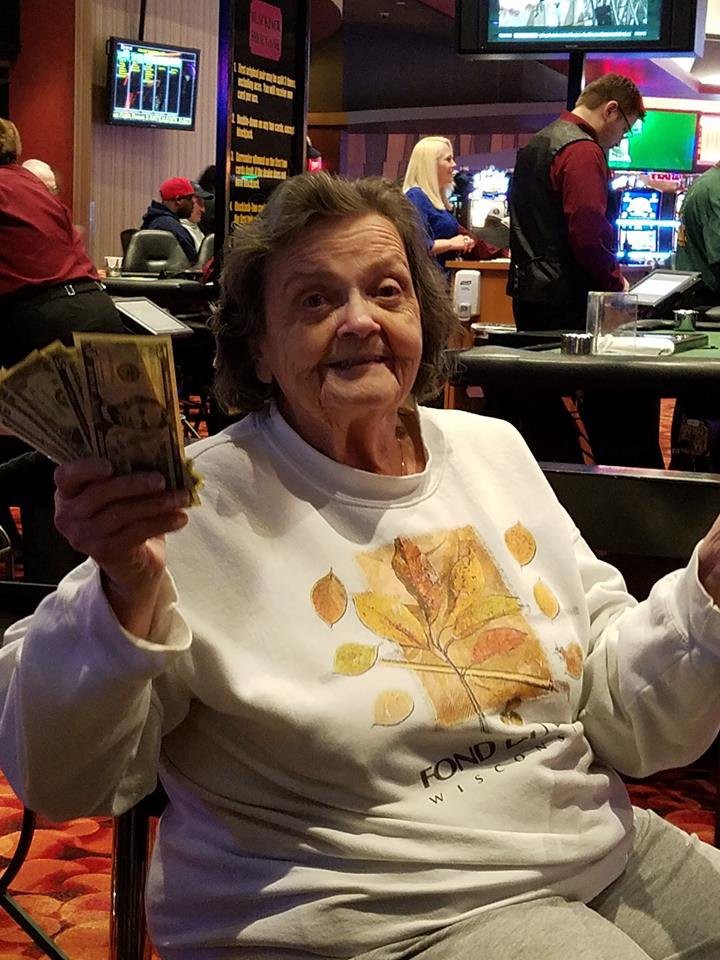 An elderly woman smiling and holding cash in a casino.