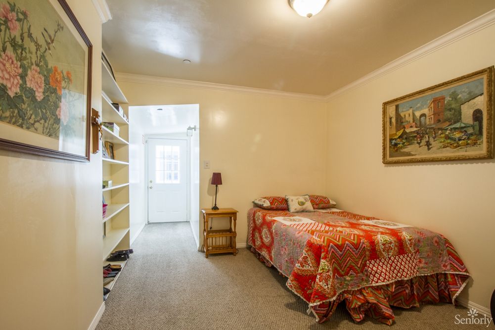 A cozy bedroom with a colorful bedspread, shelves, and artwork on the wall.