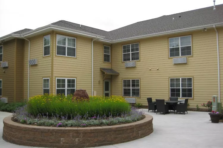 A two-story yellow house with a landscaped garden and patio area.