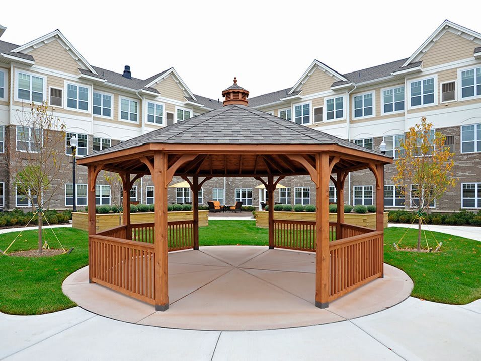 A wooden gazebo situated in the garden area of a residential building.