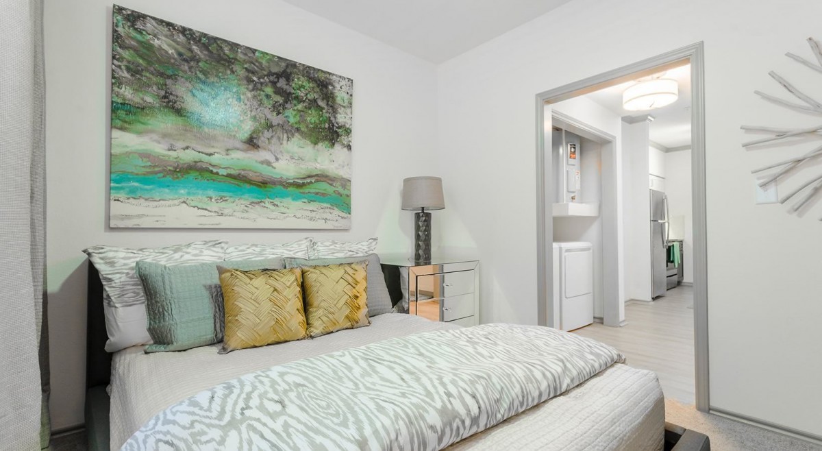 A modern bedroom with stylish decor, featuring a bed with patterned bedding, decorative pillows, and a large artwork piece above the headboard.