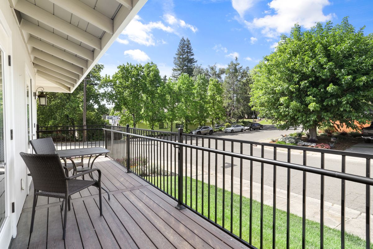 A scenic balcony with outdoor seating overlooks a lush, tree-lined street.