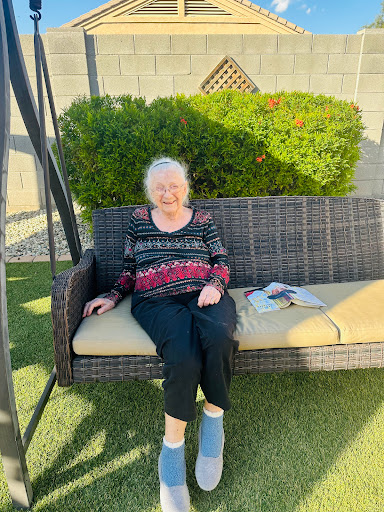 An elderly woman enjoying a sunny day on a swing in her backyard.