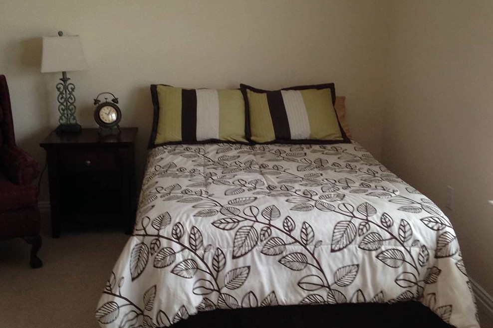 A neatly arranged bed with patterned bedding and decorative pillows, accompanied by a nightstand with an alarm clock.