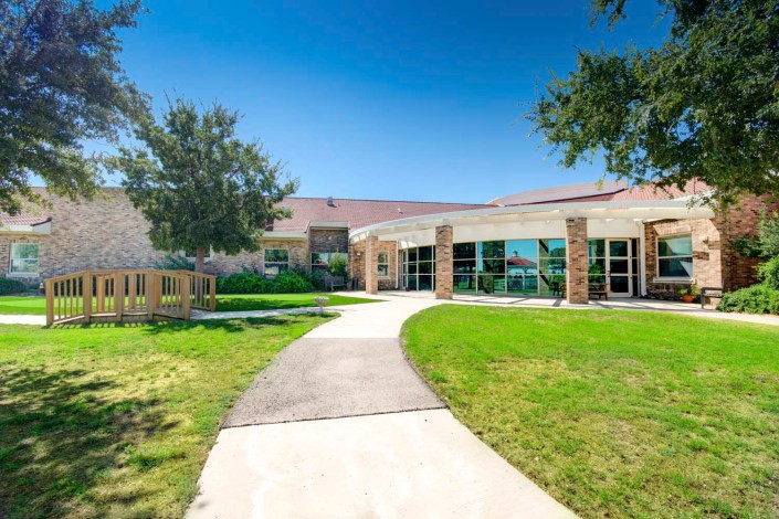 A modern building with a glass facade surrounded by a well-maintained lawn and trees under a clear blue sky.