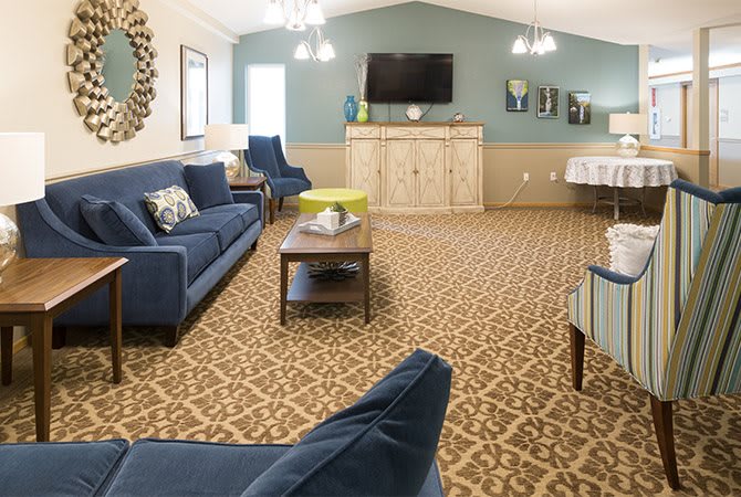 A cozy living room featuring blue sofas, patterned carpet, and a wall-mounted television.