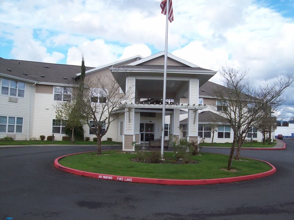 A large building with an American flag at the entrance, featuring a circular driveway and landscaped greenery.