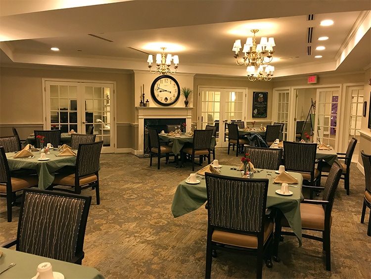 A cozy dining room with tables and chairs, featuring a fireplace and a large clock on the wall.