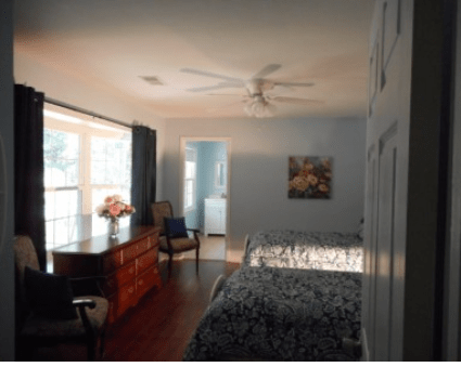 A cozy bedroom with natural light, featuring a bed, dresser, and artwork on the wall.