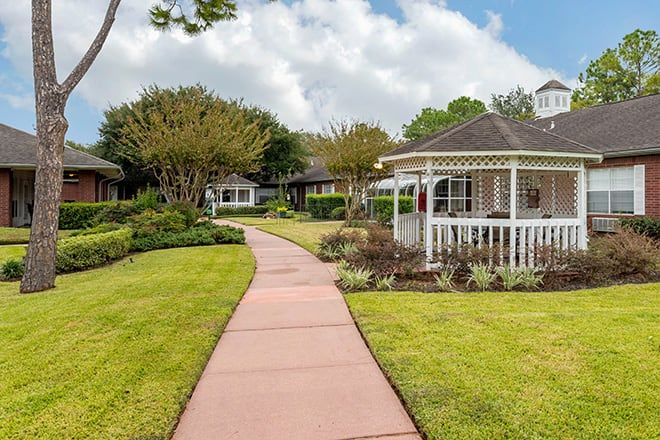 A peaceful garden featuring a walkway leading to a gazebo, surrounded by lush greenery and trees.