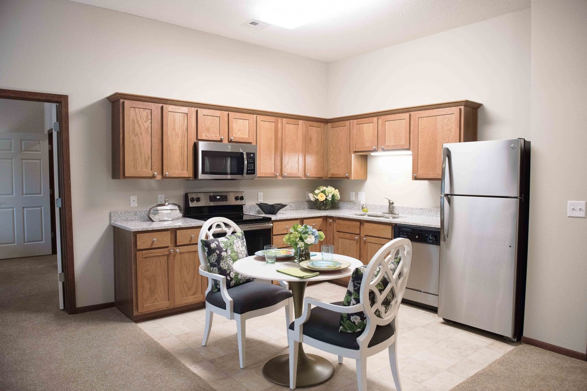 A modern kitchen with wooden cabinets, stainless steel appliances, and a small dining table with two chairs.