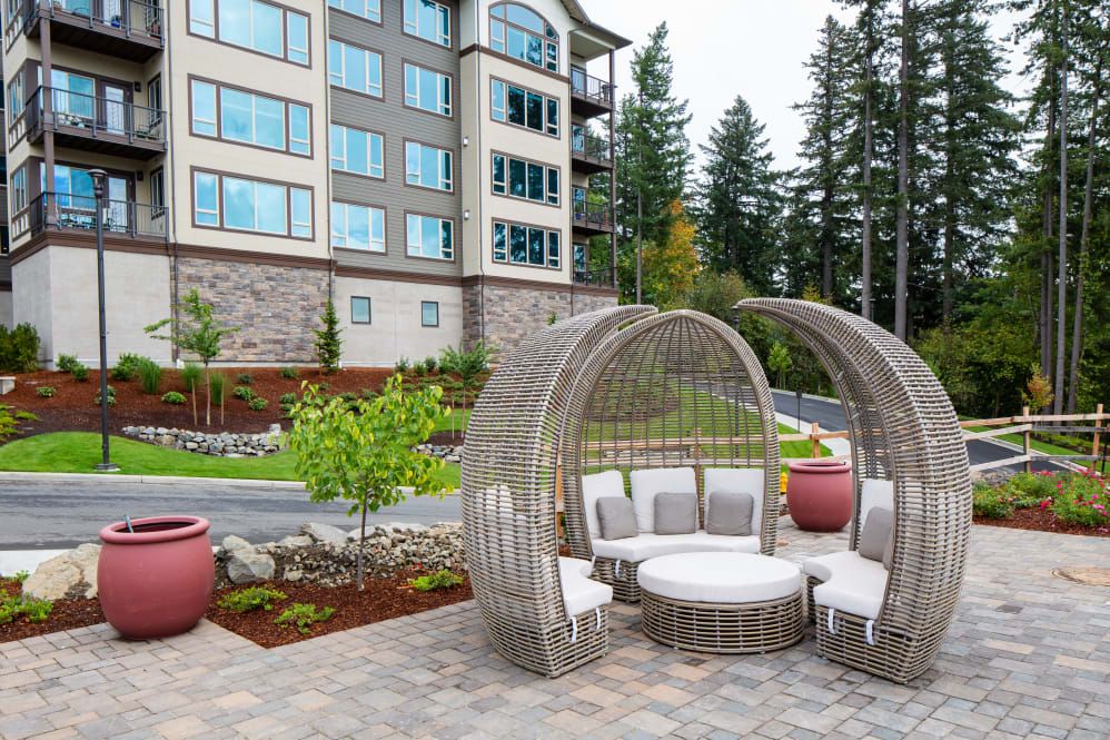 A modern outdoor seating area with stylish furniture in front of an apartment building, set amidst landscaped greenery.