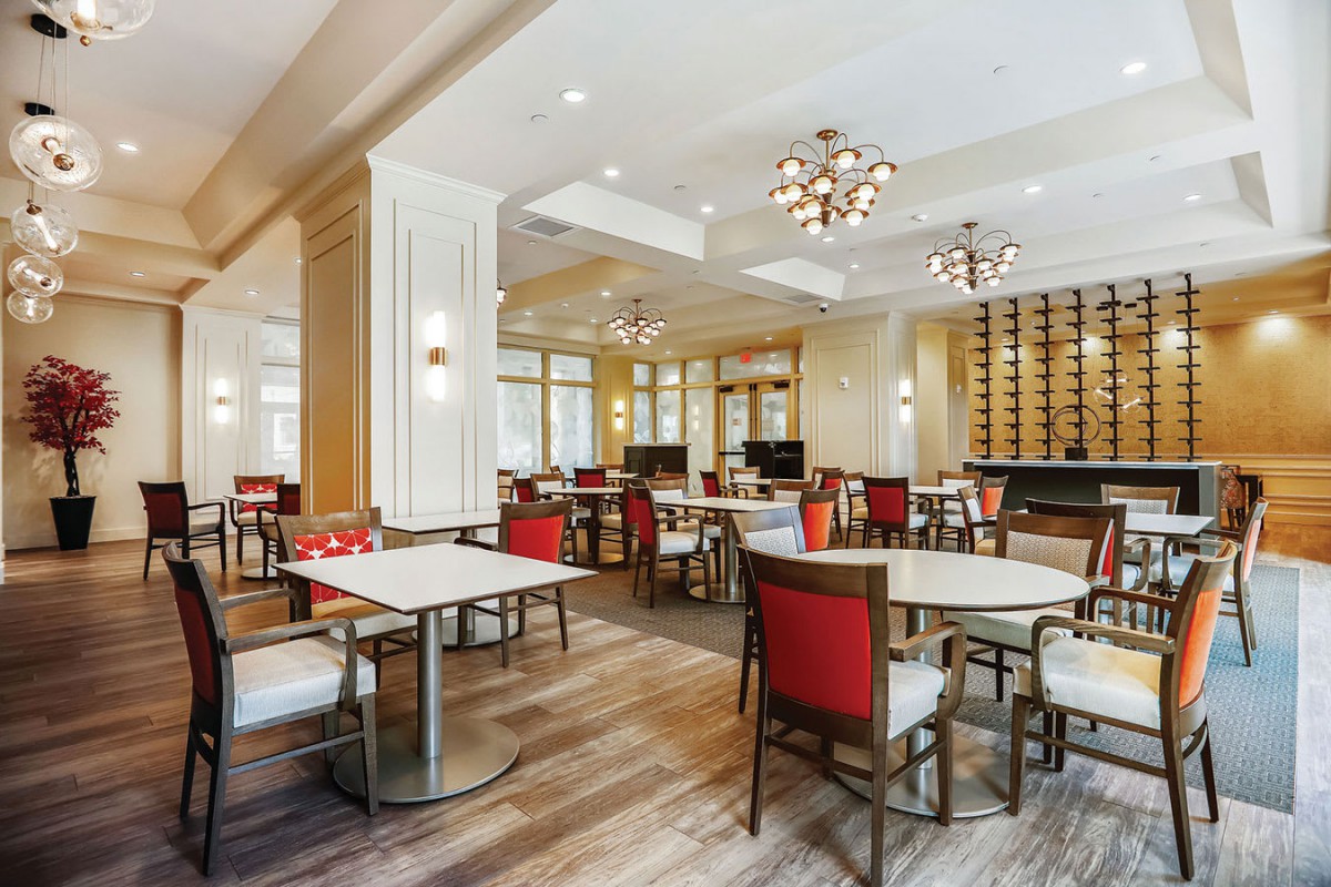 A modern restaurant interior with elegantly arranged tables and chairs, featuring stylish lighting fixtures.