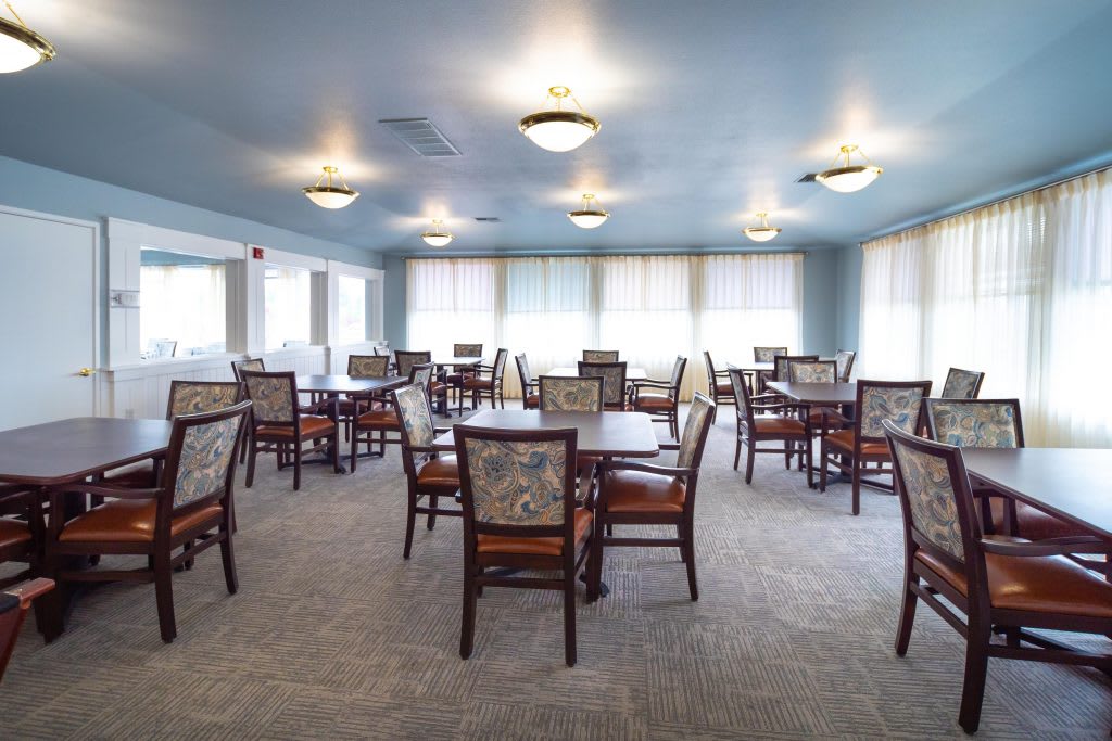 A spacious dining room with multiple tables and chairs, well-lit by ceiling lights.